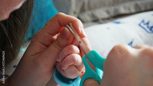 A newborn child s nails are cut with special baby scissors. An adult hand holds a small child s hand. Carefully  the mother cuts her daughter s nails. A child in a cocoon  home environment. Trust.