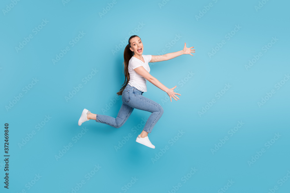 Full length profile side photo of energetic girl greet her friend jump run hug open hands wear white t-shirt gumshoes isolated over blue color background Full length profile side photo of energetic girl greet her friend jump run hug open hands wear white t-shirt gumshoes isolated over blue color background