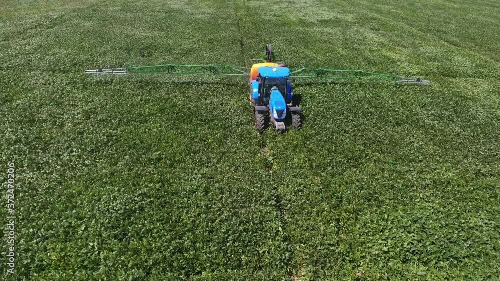 Aerial shot of huge green rice land and a riding tractor with sprinkling equipment in summer Aerial shot of huge green rice land and a riding tractor with sprinkling equipment in summer
