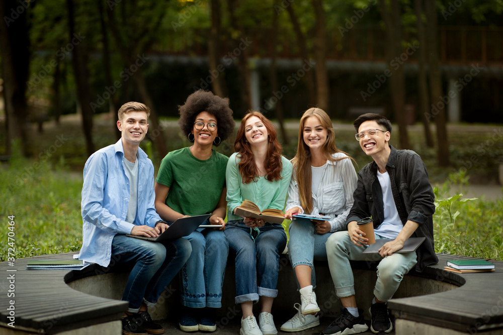 Group Of Happy Multiracial High-School Students Sitting Together On Bench In Park