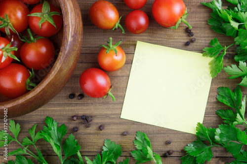 Cherry tomatoes on a wooden background with parsley, spices and a notebook for writing a recipe. Recipes concept with tomatoes, canning. Copy space