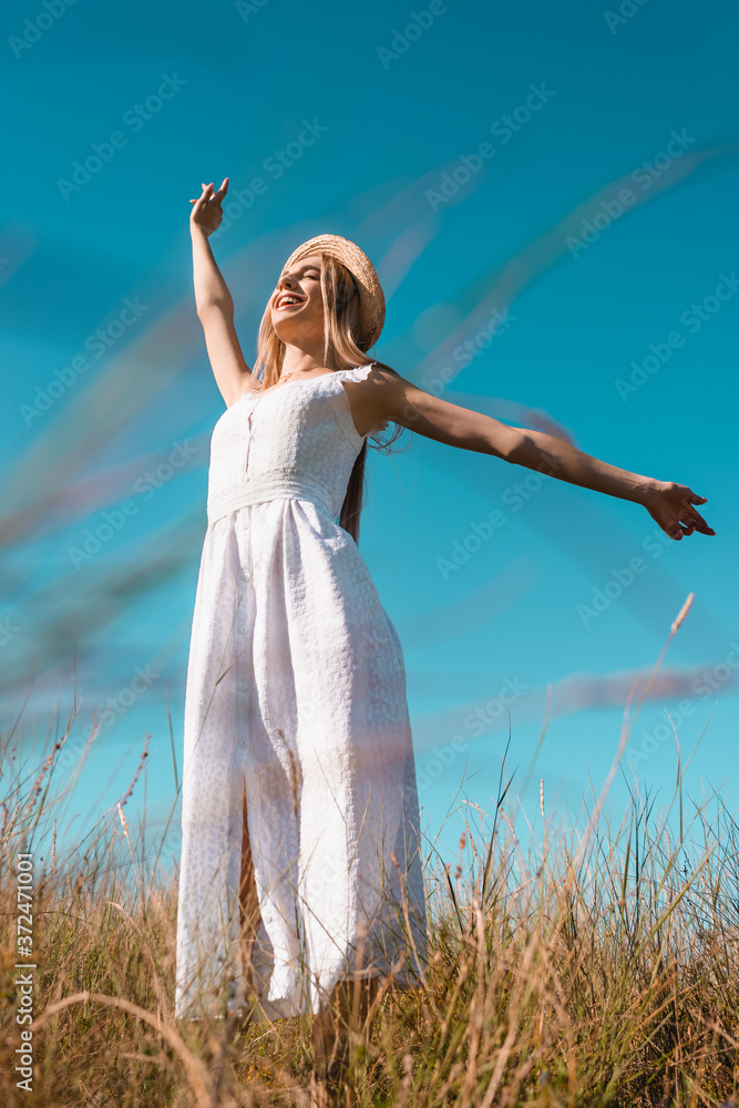 low angle view of stylish woman in white dress standing with outstretched hands and closed eyes against blue sky low angle view of stylish woman in white dress standing with outstretched hands and closed eyes against blue sky