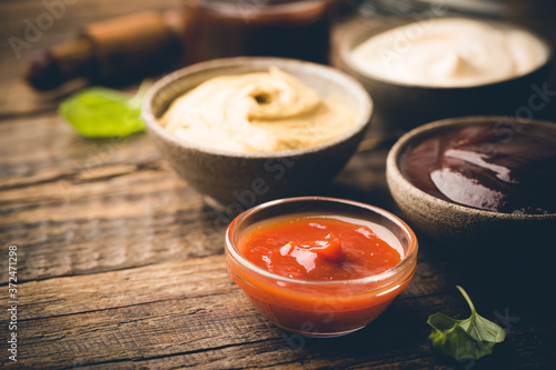 Fotografia Classic set of sauces, American yellow mustard, ketchup, barbecue sauce, mayonnaise on wooden background, top view with copy space