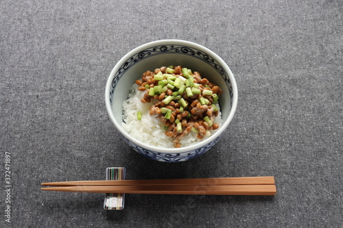 Natto, fermented soybeans on steamed rice in bowl and wooden chopstics on table