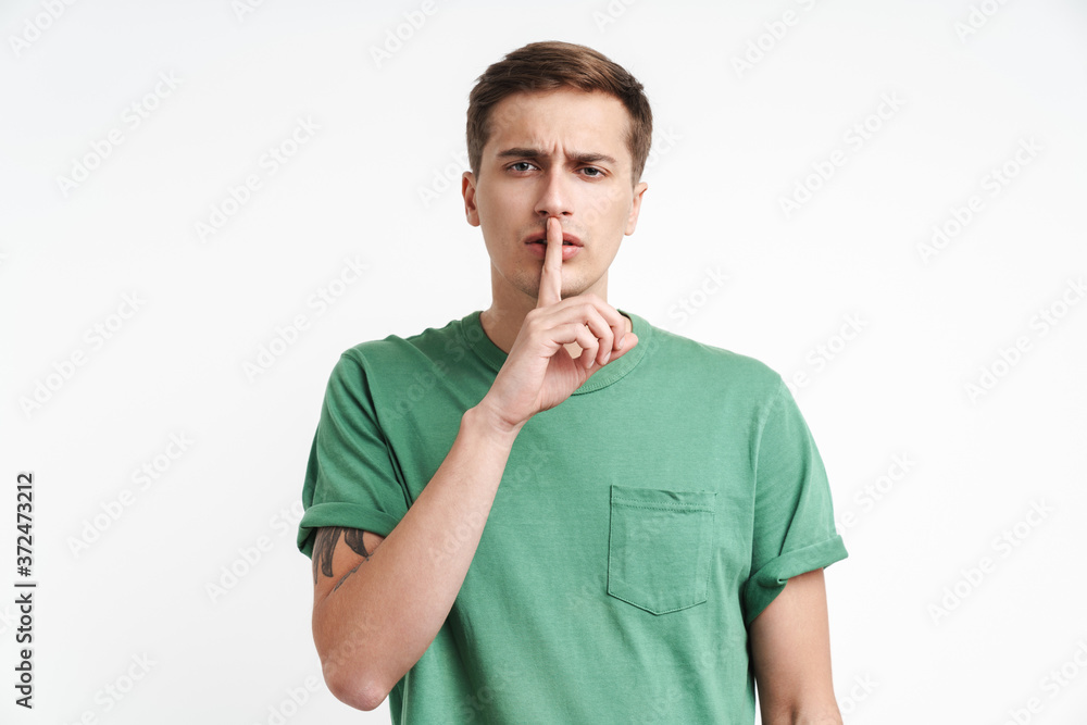 Image of attractive man in basic t-shirt holding index finger at lips Image of attractive man in basic t-shirt holding index finger at lips