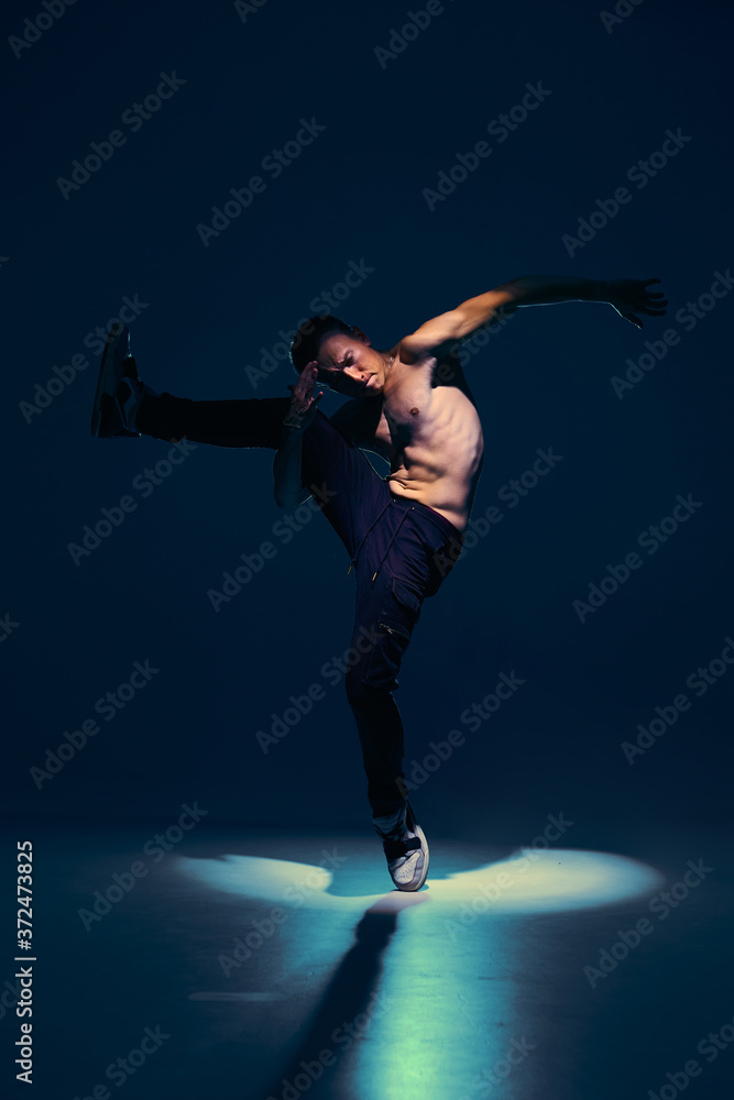 Young guy dancer with naked torso dancing in studio in spotlight on black background. Dance school poster