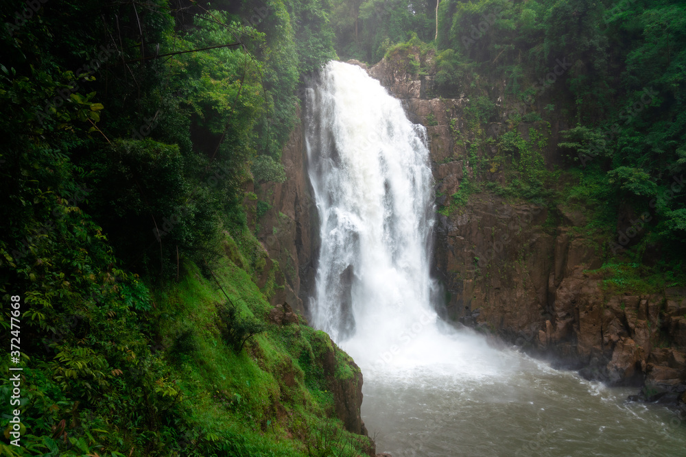 Beautiful enormous waterfall with severe stream that flowing down from high mountain cliff. Photo contained noise due to stream's vapor splashing from severe flow condition. Beautiful enormous waterfall with severe stream that flowing down from high mountain cliff. Photo contained noise due to stream's vapor splashing from severe flow condition.