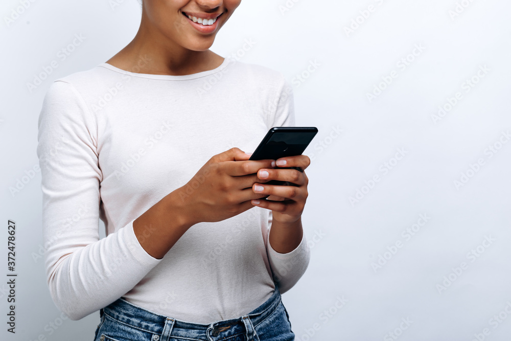 Cute, smiling girl with a phone in his hands on a background of a white wall, close-up view Cute, smiling girl with a phone in his hands on a background of a white wall, close-up view