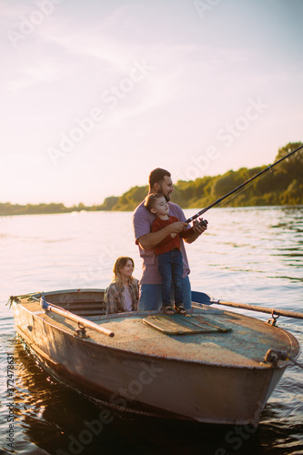 Happy family fishing on boat on river in summertime. Father teaches son fishing. Photo for blog about family travel