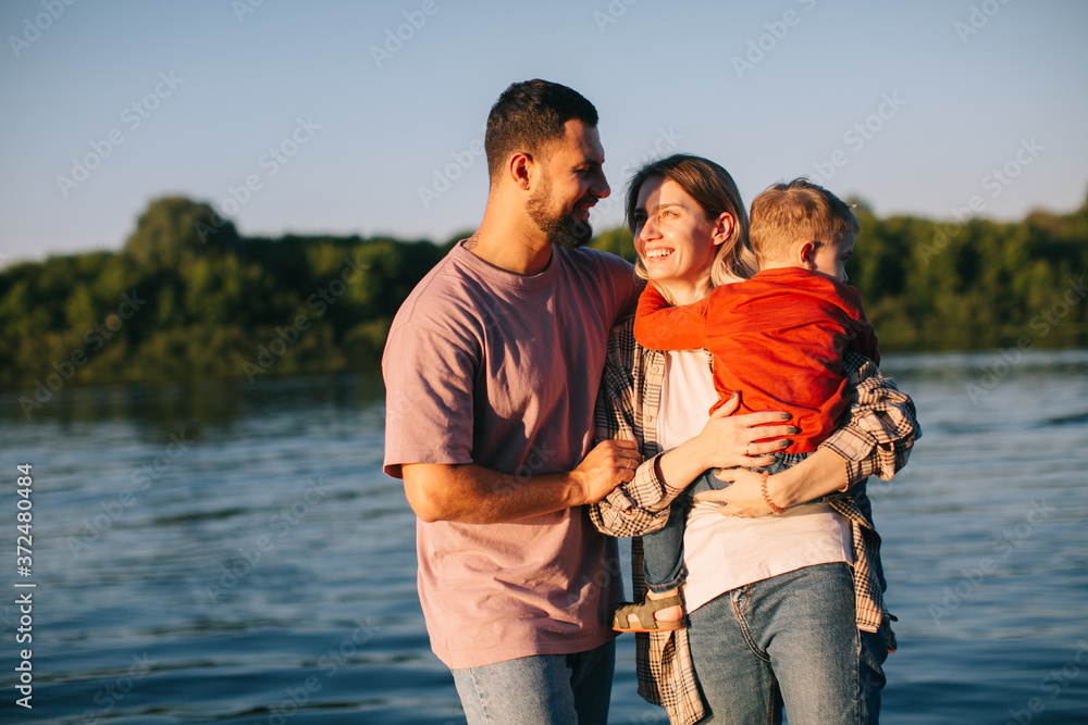 Young family hug each other on river background. Summer photography for blog or advertising about family and travel Young family hug each other on river background. Summer photography for blog or advertising about family and travel