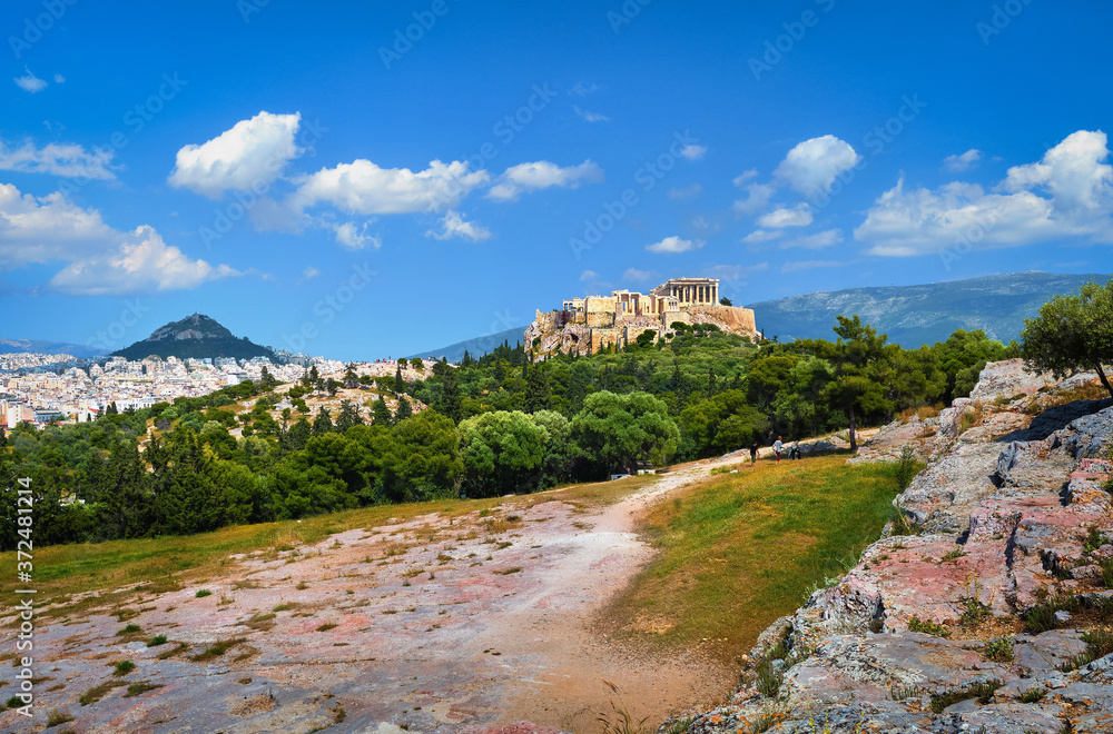 Beautiful view of Acropolis hill and Lycabettus hill in background in Athens, Greece from Pnyx hill in summer daylight with great clouds in blue sky.