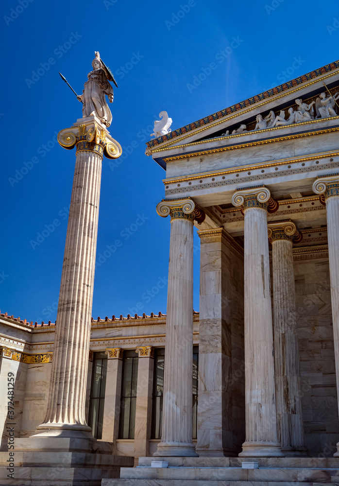 Column with statue of Athena, ancient Greek goddess, city patron, by main entrance to Academy of Athens, Greece, on summer day at blue sky