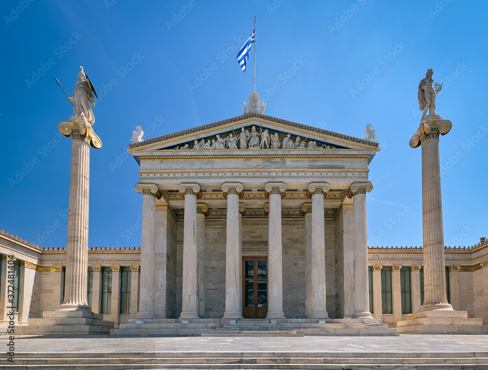 Main entrance of Academy of Athens, national research center, columns with Athena, ancient Greek goddess, and Apollo, ancient Greek god. Greek flag