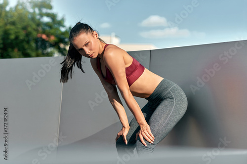Sporty young woman resting after stretching exercises in the city street. Fitness girl relaxing outside on a sunny day after pilates training outside.