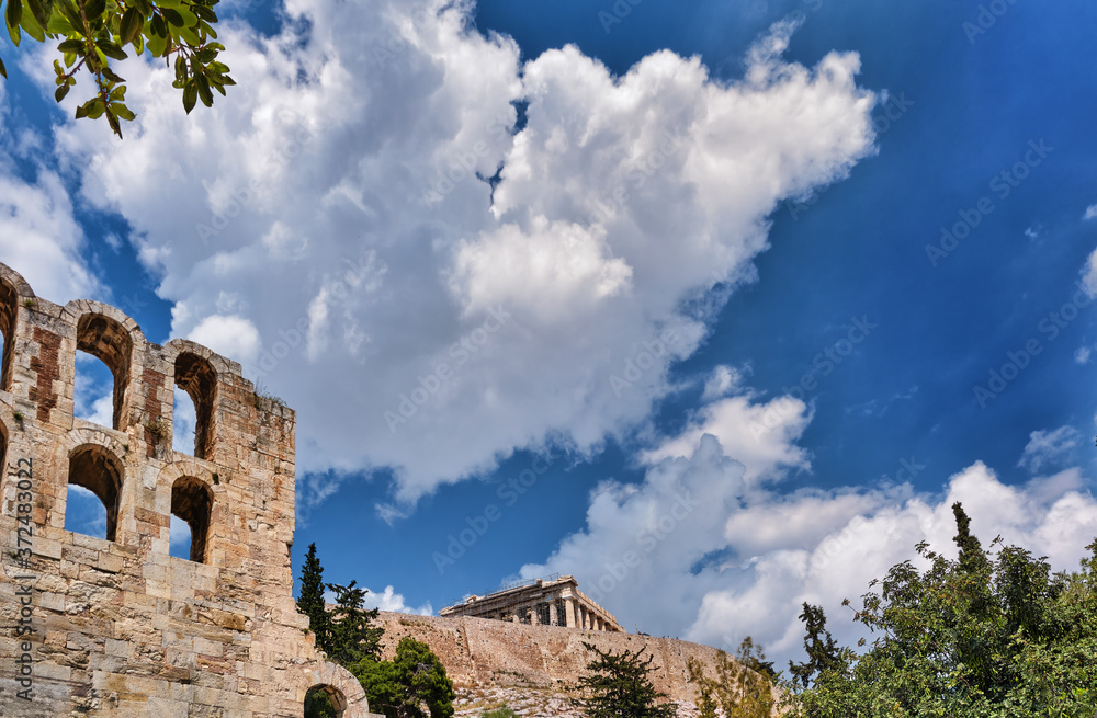 View of Odeon of Herodes Atticus theater on Acropolis hill, Athens, Greece, at bright blue sky and super clouds. Classic ancient Greek theater ruins