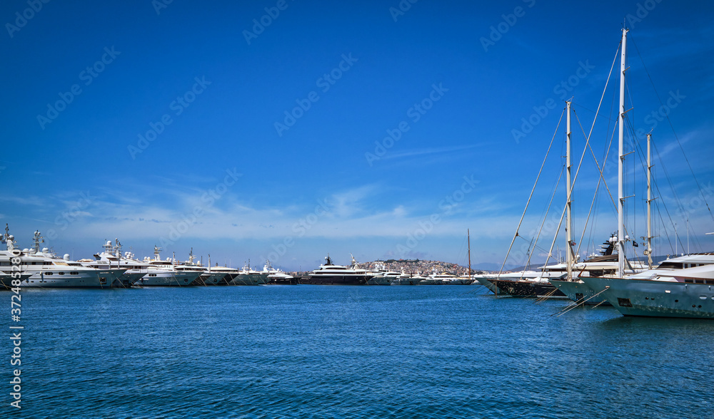Boats and yachts anchored or moored in a marina and by its promenade on a bright summer day. Beautiful seascape. Leisure, cruise, vacation. 