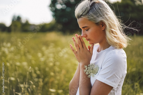 Girl closed her eyes, praying in a field.  Hands folded in prayer concept for faith