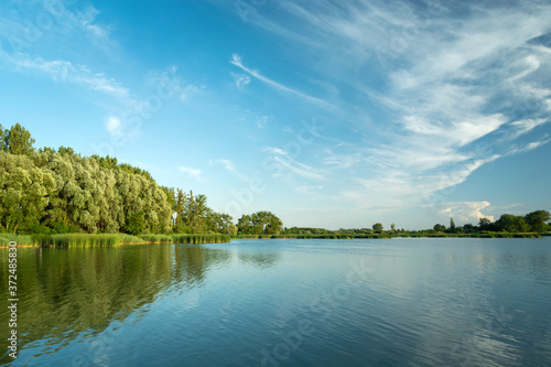 Cirrus clouds in the blue sky over a lake and a green forest, Stankow, Poland