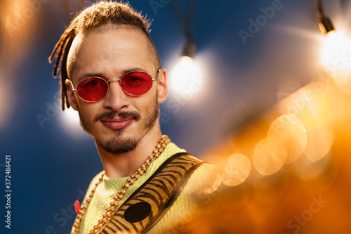 Young fashionable man in pink sunglasses playing guitar with joy