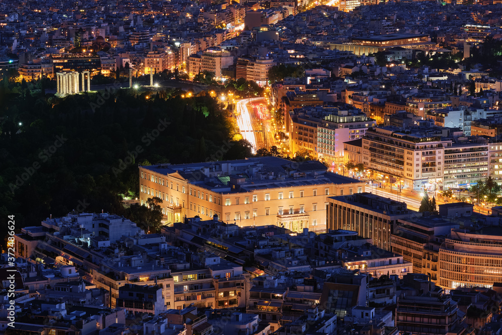 Night view Hellenic Parliament in Syntagma square brightly lit up and ruins of temple of Olympian Zeus behind it shot from hill of Lycabettus,