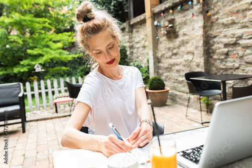 Senior female blogger in casual wear sitting in cafe using laptop.