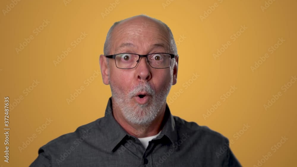 Slow motion closeup of man shocked, saying WOW. Handsome guy with bald gray hair surprised to camera on orange background. Slow motion closeup of man shocked, saying WOW. Handsome guy with bald gray hair surprised to camera on orange background.