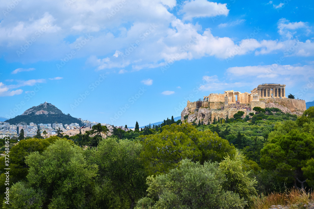 Iconic vew of Acropolis hill and Lycabettus hill in background in Athens, Greece from Pnyx hill in summer daylight with great clouds in blue sky.