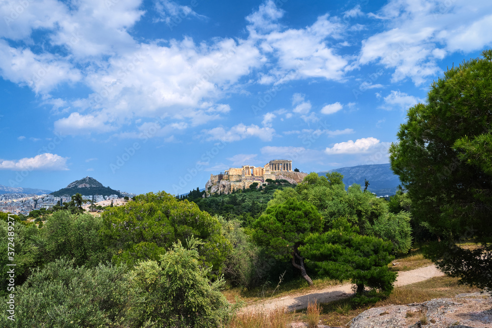 Iconic view of Acropolis hill and Lycabettus hill in background in Athens, Greece from Pnyx hill in summer daylight with great clouds in blue sky.