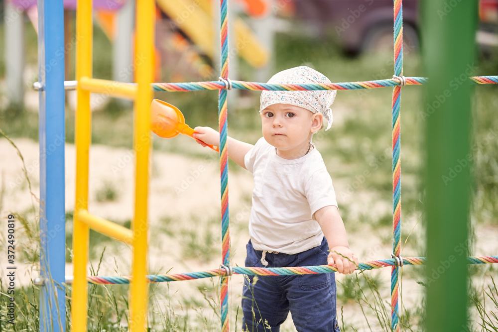 Obraz premium A cute child in a bandana is holding on to the stairs in the playground.