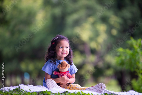 A cute girl is sitting on a white carpet in the park on a relaxing day and happy smiling.