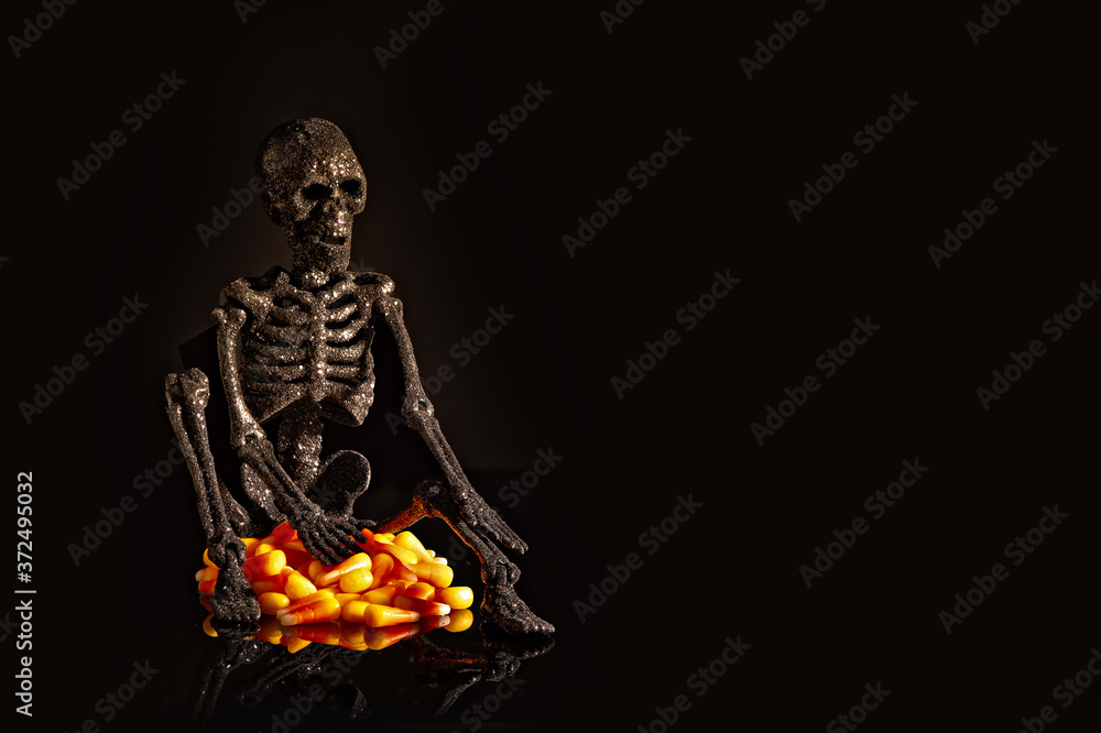 Spooky halloween skeleton sitting on candy corn, black background Spooky halloween skeleton sitting on candy corn, black background