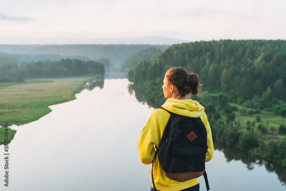 Young woman girl traveler in yellow hoodie with backpack looking at sunrise on the beautiful view. Local tourism, weekend trip Young woman girl traveler in yellow hoodie with backpack looking at sunrise on the beautiful view. Local tourism, weekend trip