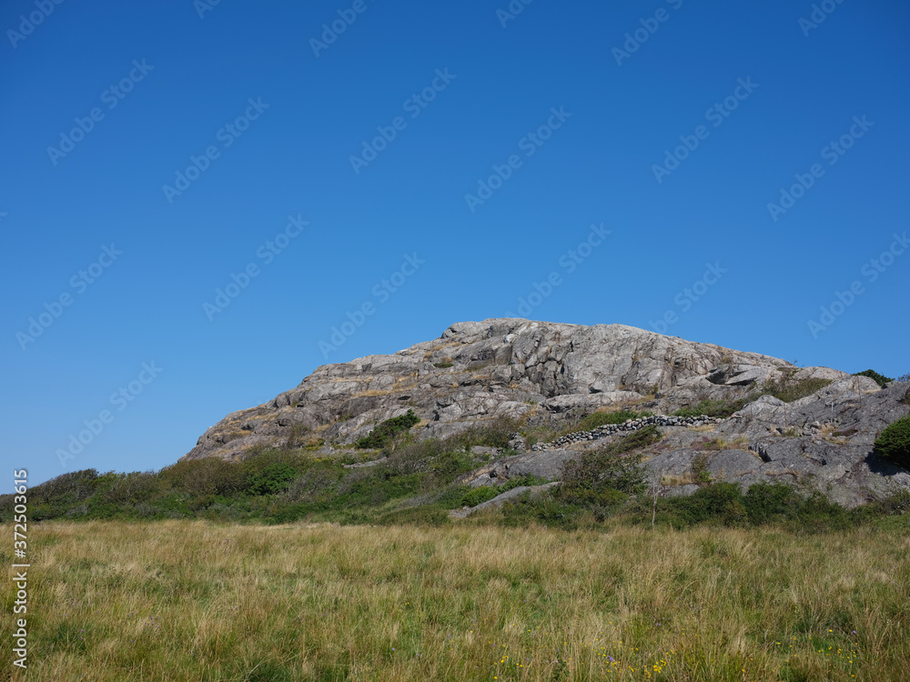 Rocky hill with a stone fence and pasture land in the foreground. Shot on a clear summers day against blue sky.