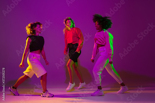 Flexible. Sportive girls dancing hip-hop in stylish clothes on purple-pink background at dance hall in green neon light. Youth culture  movement  style and fashion  action. Fashionable portrait.