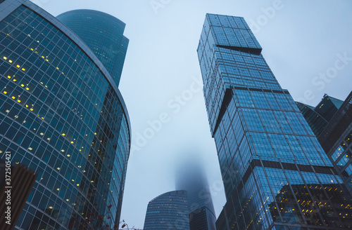 Skyscrapers of the office center made of glass and concrete in clouds of thick fog.
