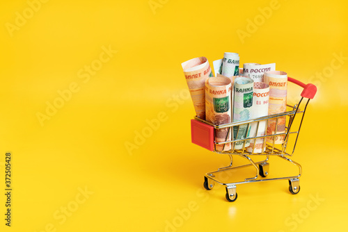 Russian ruble banknotes in shopping cart on yellow background. Economic concept of food basket value. Copy space