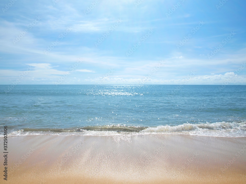 Beach and blue sky. Perfect seascape. Azure sea and bright sun above it. Wave coming back, sparkling reflection of the sun on the surface of the water, pure white sand. Wave returning from sand to sea