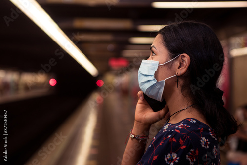 Close up latin woman talking on the smartphone and wearing face mask waiting the metro on the station.