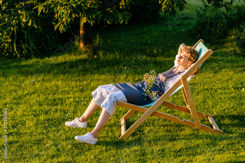 Canvas Print Beautiful smiling woman gardener in apron relaxin at sun lounger on a grass meadow outdoor