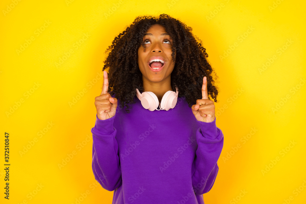 Charming carefree woman with positive expression, points up with both index fingers, dressed in casual clothing, has broad interested smile, isolated over gray background. Look there, please. Charming carefree woman with positive expression, points up with both index fingers, dressed in casual clothing, has broad interested smile, isolated over gray background. Look there, please.
