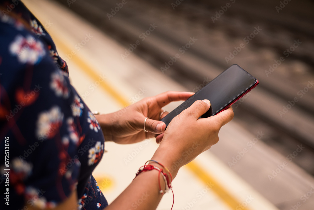 Hand woman waiting on subway platform with her cell phone. Blurred railway on the background.