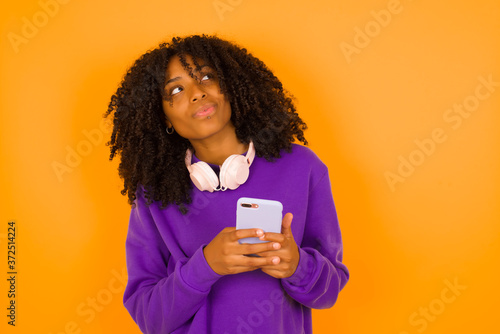 Image of a happy young beautiful woman posing isolated over bright background listening to music with earphones using mobile phone.