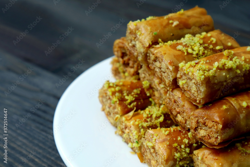 Closeup Pile of Mouthwatering Baklava Pastries with Pistachio Nuts on a White Plate Closeup Pile of Mouthwatering Baklava Pastries with Pistachio Nuts on a White Plate