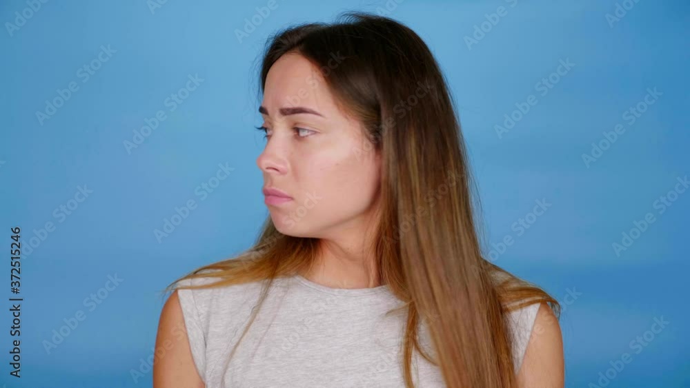 Sad woman in gray t-shirt looks around raises hands does not know what to choose on blue background with copy space. 4K slow motion footage Sad woman in gray t-shirt looks around raises hands does not know what to choose on blue background with copy space. 4K slow motion footage
