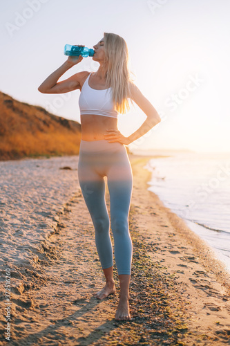 woman in tracksuit by the sea drinks water after workout