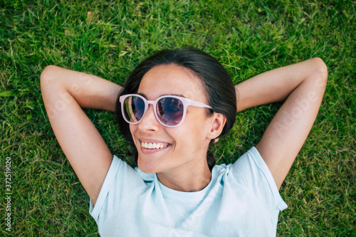 Happy beautiful hipster woman in cool sunglasses is having fun while she is lying on the lawn and looking on camera © My Ocean studio