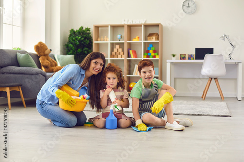 Happy mother and children in household gloves sitting on floor and looking at camera