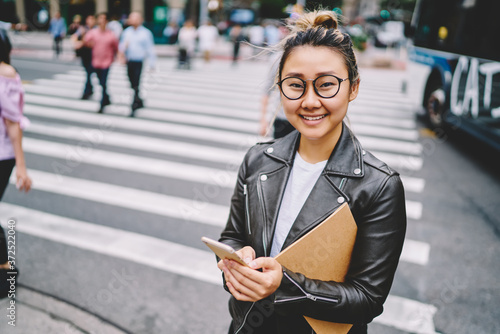 Half length portrait of beautiful prosperous asian woman strolling at urban city setting and using modern technology.Cute cheerful hipster girl looking at camera while sending messages to friends