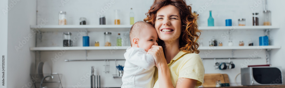 panoramic shot of young mother with closed eyes holding infant boy in kitchen panoramic shot of young mother with closed eyes holding infant boy in kitchen
