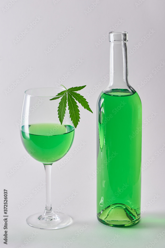 A glass and a bottle of marijuana-infused wine on white background. A glass and a bottle of marijuana-infused wine on white background.